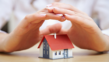two hands covering a small house model
